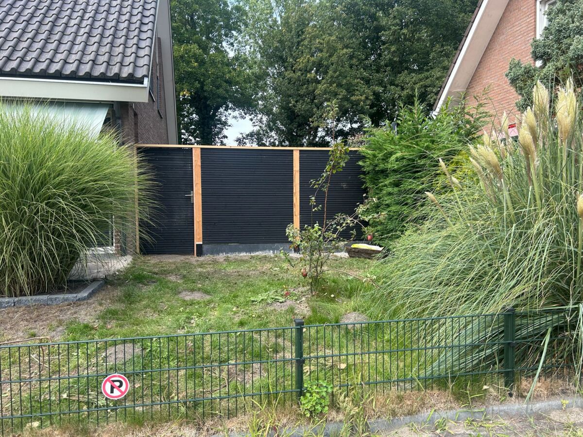 Schutting met antracieten panelen en houten palen in een aangelegde tuin